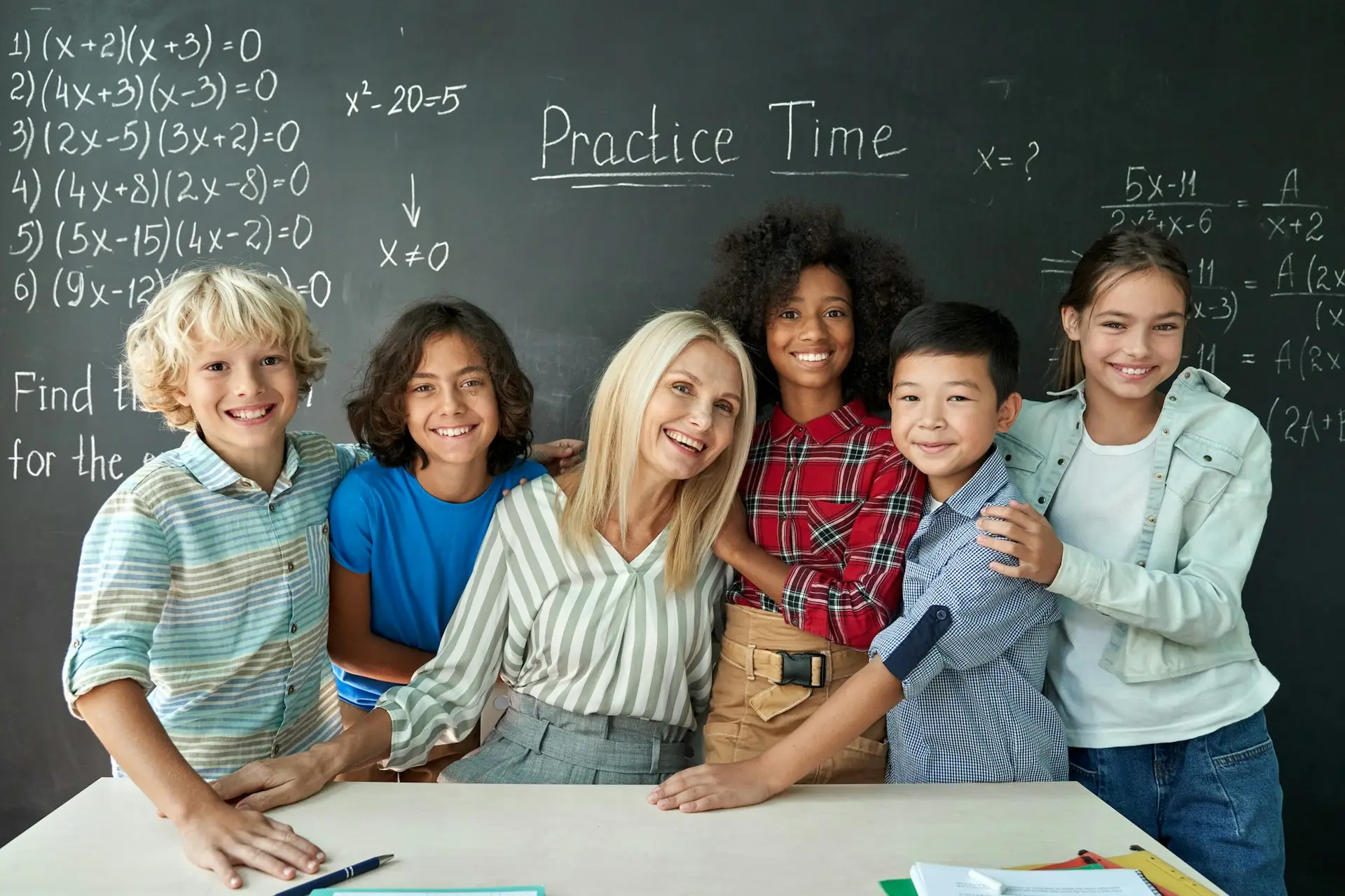 Portrait of cheerful smiling teacher and diverse schoolkids near chalkboard.