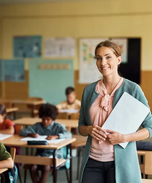 Happy elementary school teacher in the classroom looking at camera.