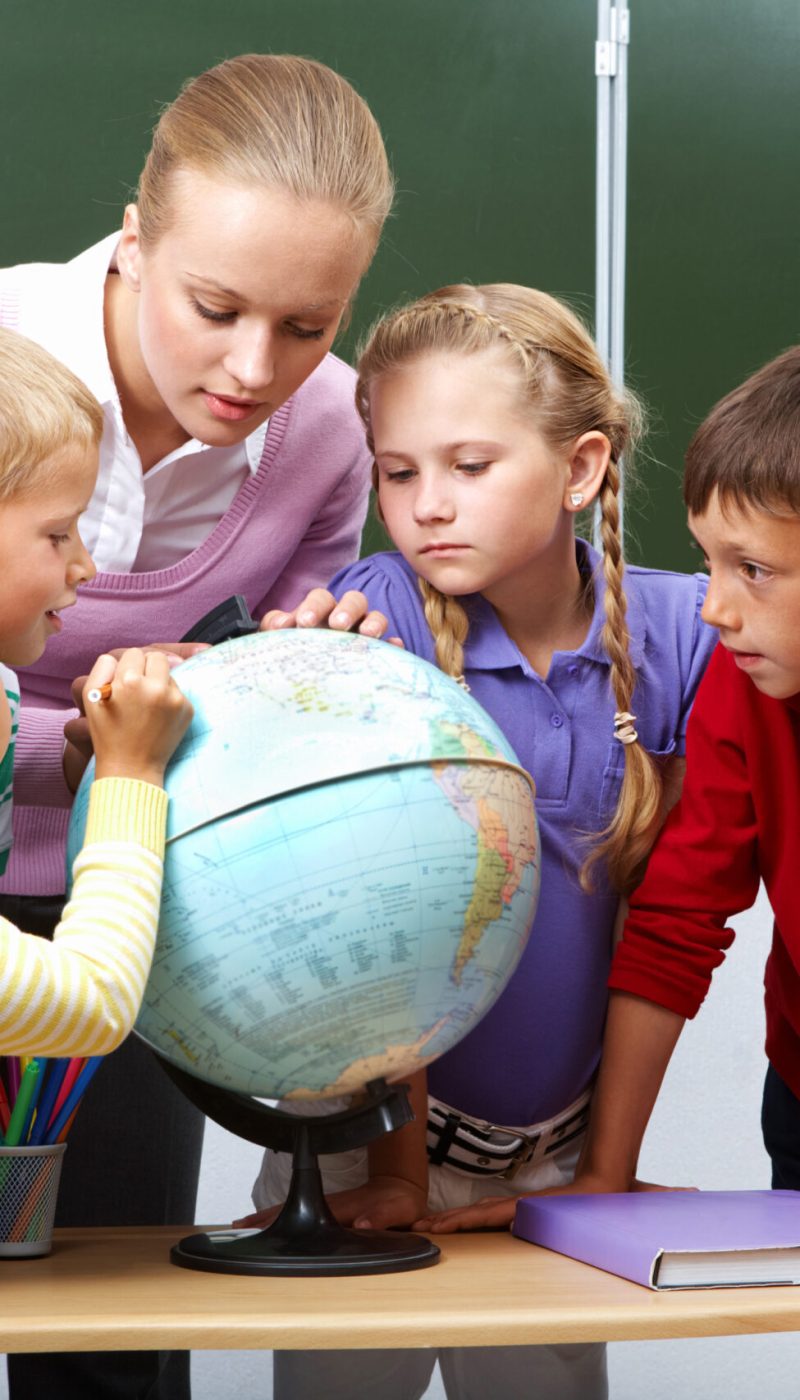 Portrait of pupils looking at globe while listening to teacher during geography lesson